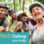 A photo of four people riding bikes posing for a selfie. With the text "The Bike Month Challenge" over it.