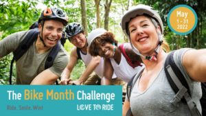 A photo of four people riding bikes posing for a selfie. With the text "The Bike Month Challenge" over it.