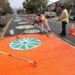 Workers apply orange coating along 90th Avenue in East Oakland, California